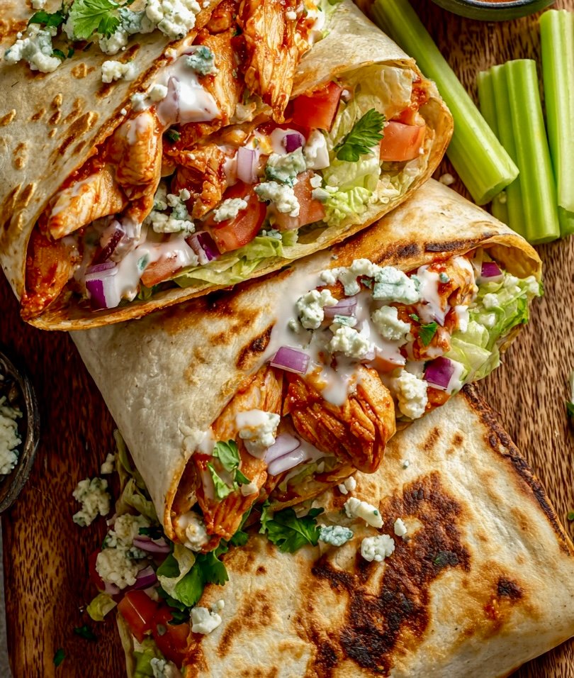 30-Minute Buffalo Wrap. A golden-brown buffalo chicken wrap sliced in half on a rustic plate, garnished with celery and blue cheese crumbles.