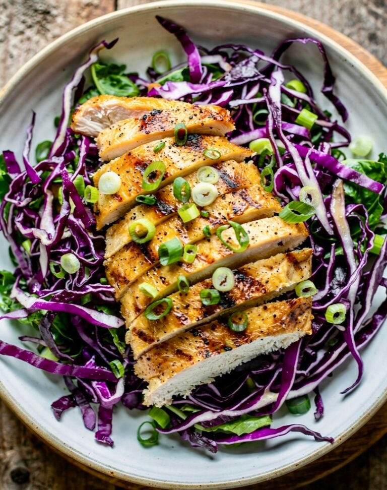 Sliced grilled chicken breast served over a vibrant purple red cabbage salad with cilantro garnish.