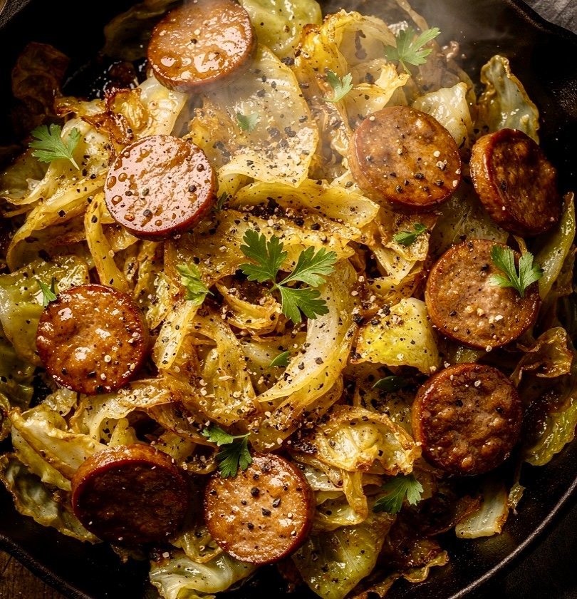 A sizzling skillet fried cabbage with browned sausage slices and tender fried cabbage.