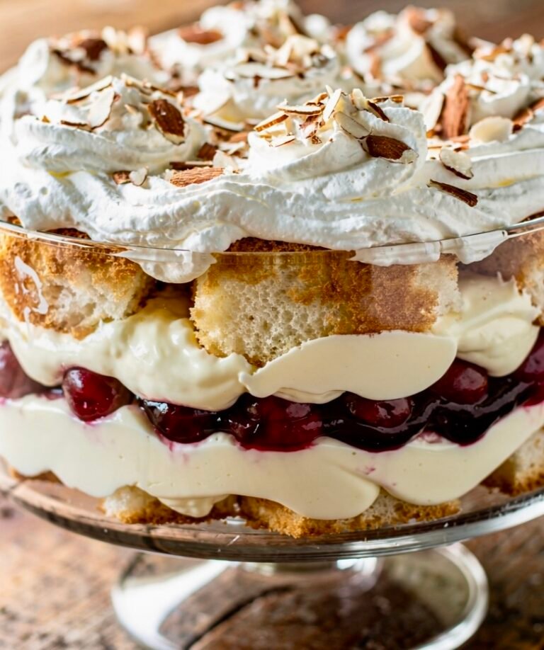 Layered Heaven on Earth Cake in a glass trifle dish with angel food cake, vanilla pudding, cherry pie filling, whipped cream, and toasted almonds