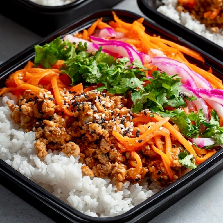 Banh Mi Chicken Bowls . A black meal prep container filled with fluffy white rice, savory ground chicken, bright orange carrots, fresh green cilantro, and bright purple pickled red onions
